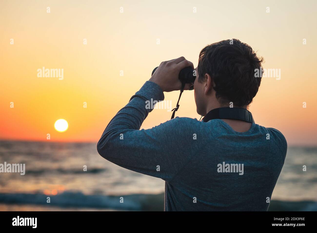 A man looking through binoculars standing on the beach Stock Photo