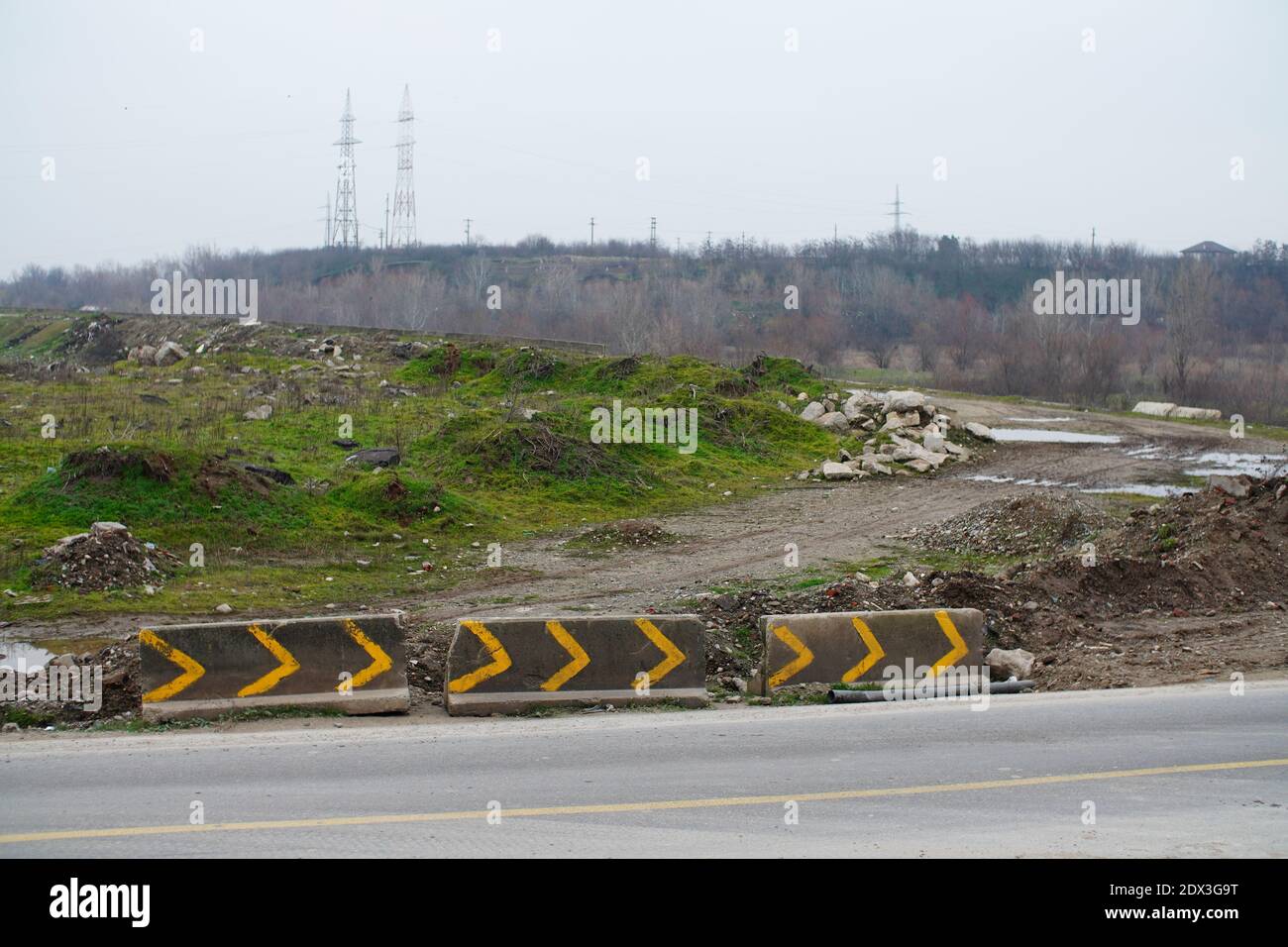 A dirt road beside a highway with painted concrete barrier Stock Photo