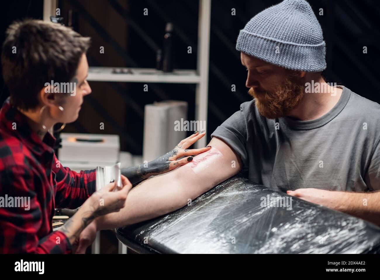 Young informal girl tattoo artist puts a bandage with vaseline on the