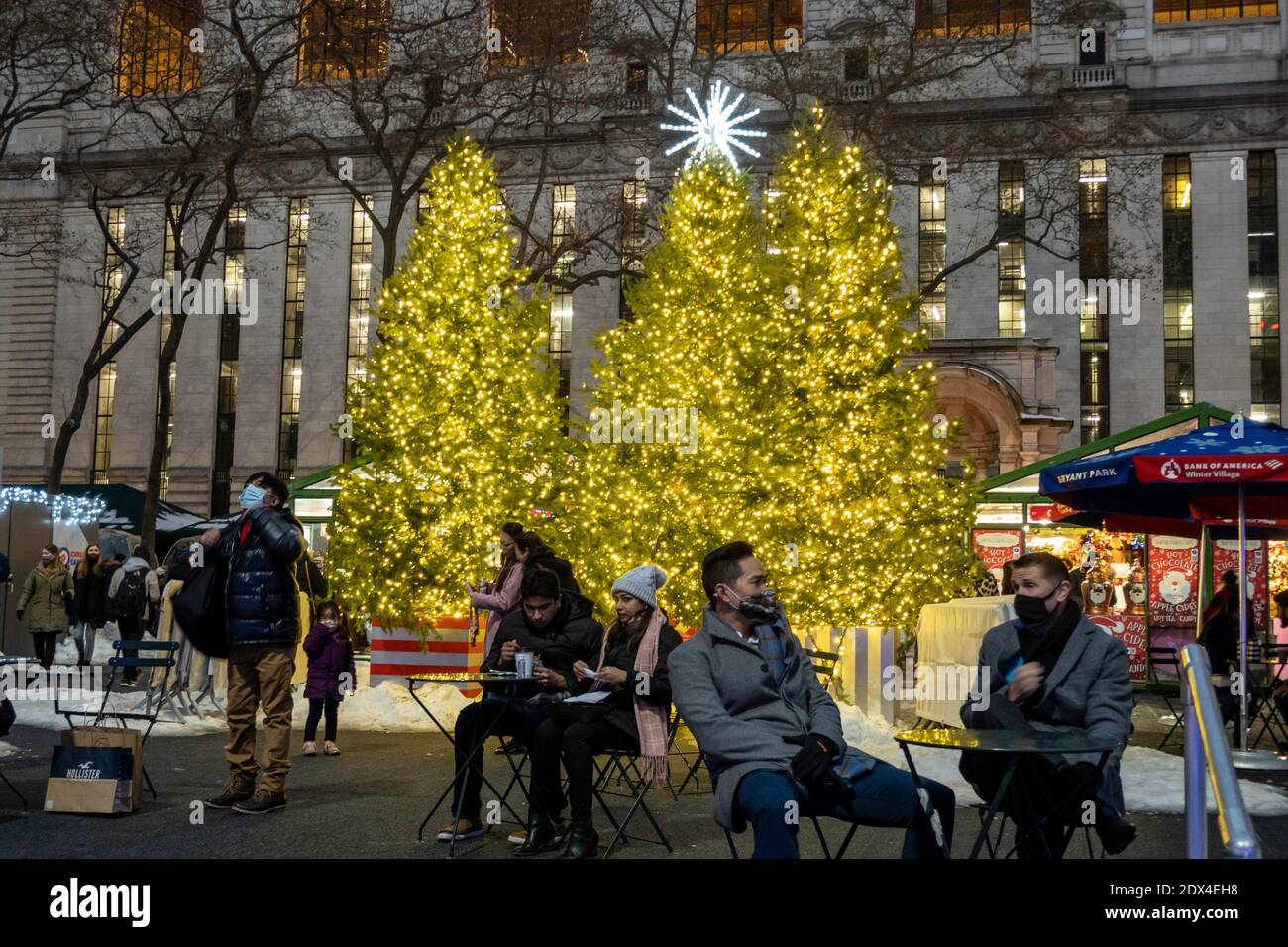 People enjoying the brightly lit Christmas trees in Bryant Park's holiday village on a wintry evening, New York City, USA Stock Photo