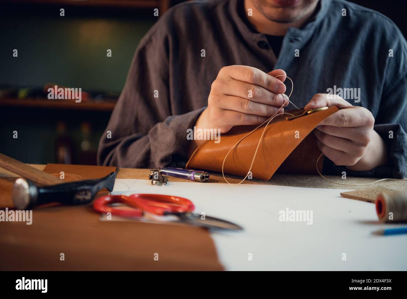 A young shoemaker manually sews decorative elements to leather shoes in the workshop. Stock Photo