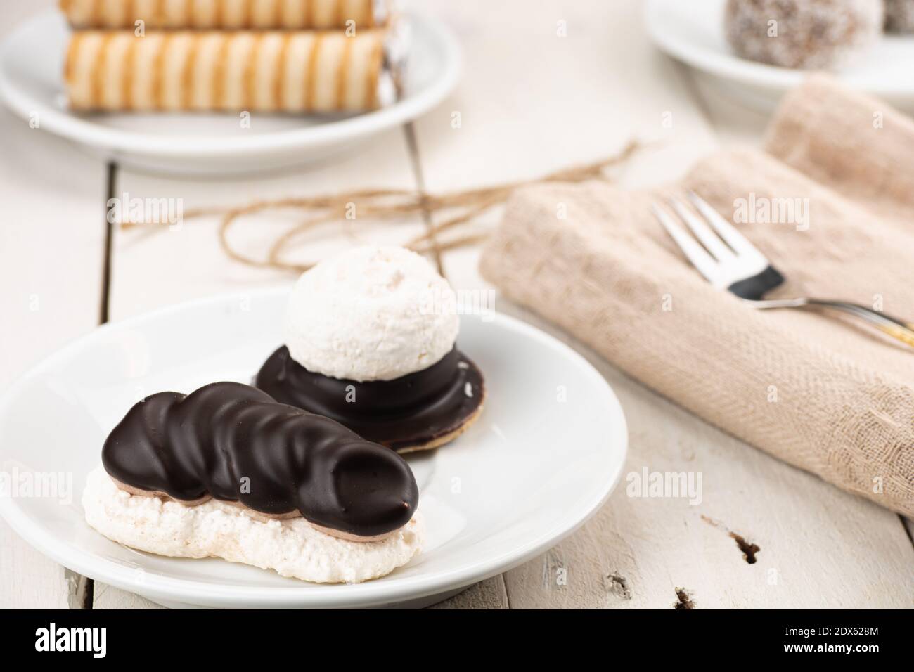 Coconut cakes with cocoa cream fill and chocolate topping. Served on wooden table and golden fork on white plate. Wedding dessert. Homemade baking Stock Photo
