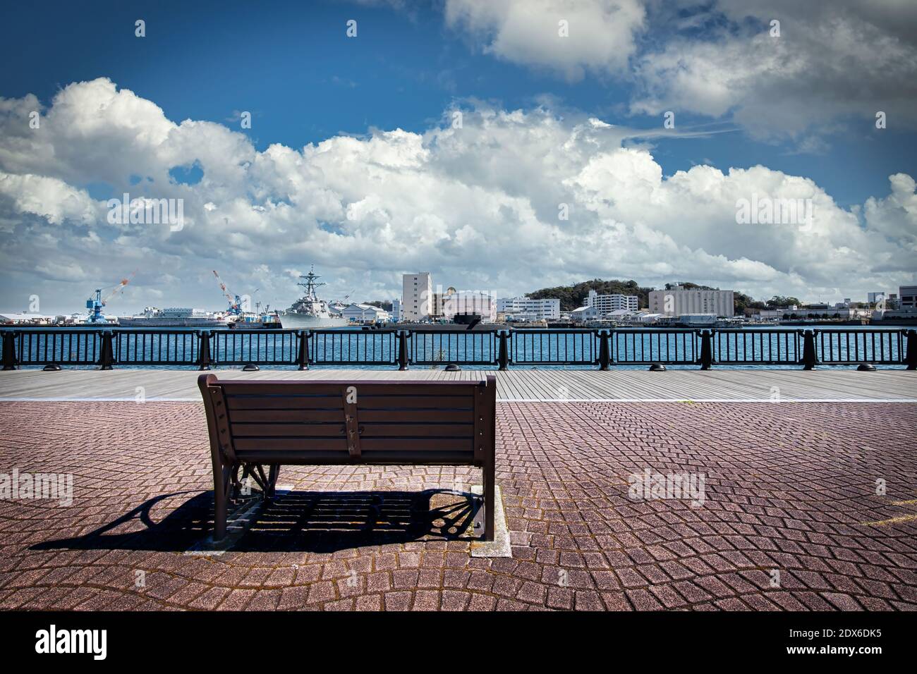 A park bench at Verny Park in Yokosuka, Japan with US ships and Japanese submarines docked in the background at the US Navy Base across the harbor. Stock Photo