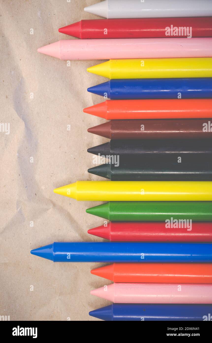 A set of lined up colored wax crayons on recycled paper background ...