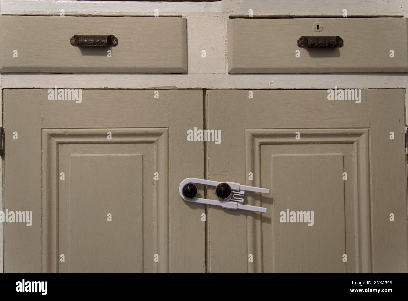 A child or baby safety locking device, holding the handles of two doors of a cabinet closed. Stock Photo