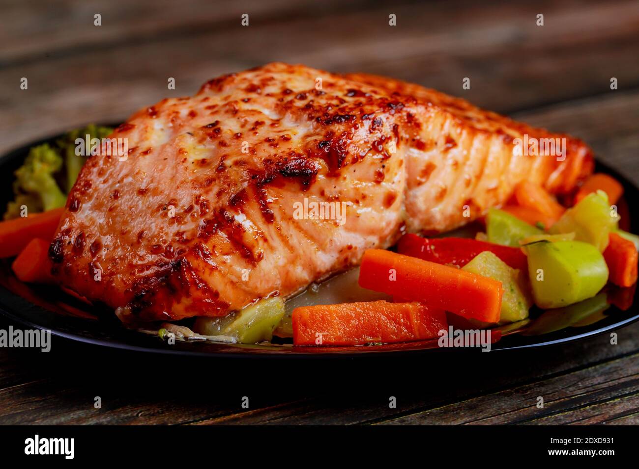 Baked juicy salmon fillet with steamed vegetables on black plate ...