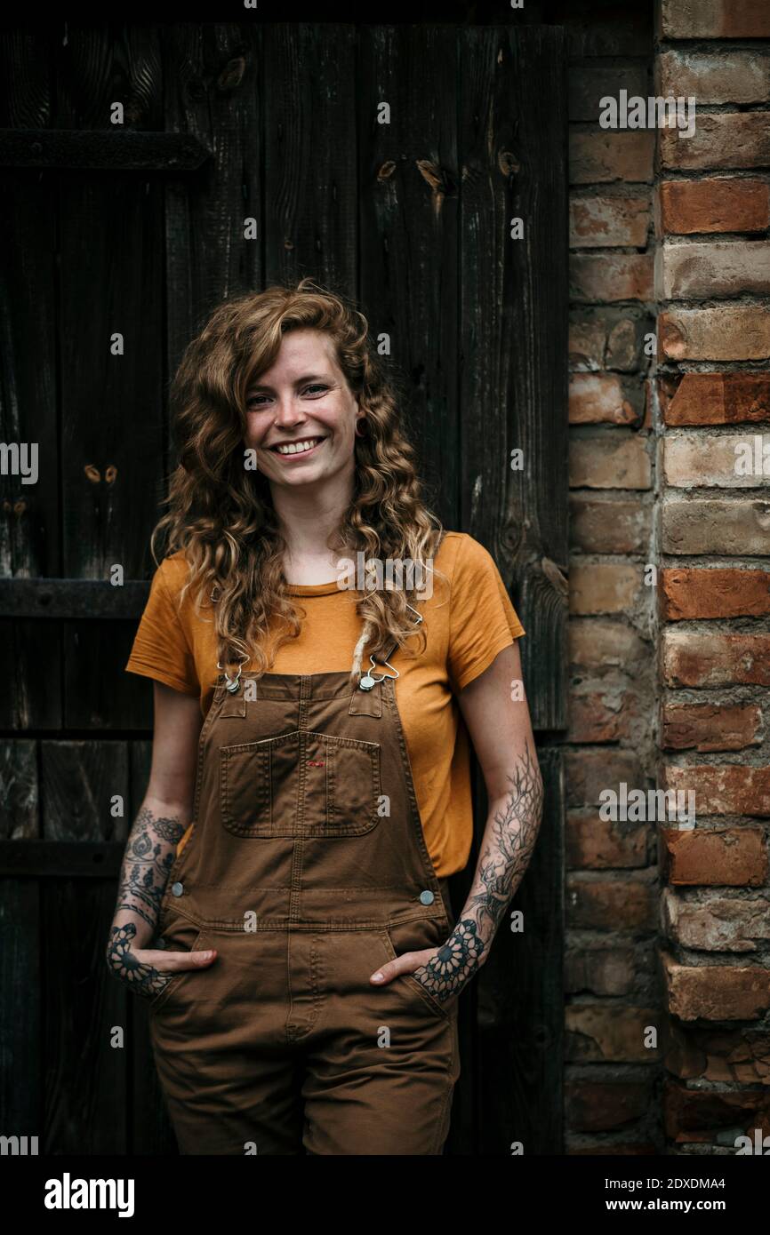 Smiling woman standing with hands in pockets against wall Stock Photo ...