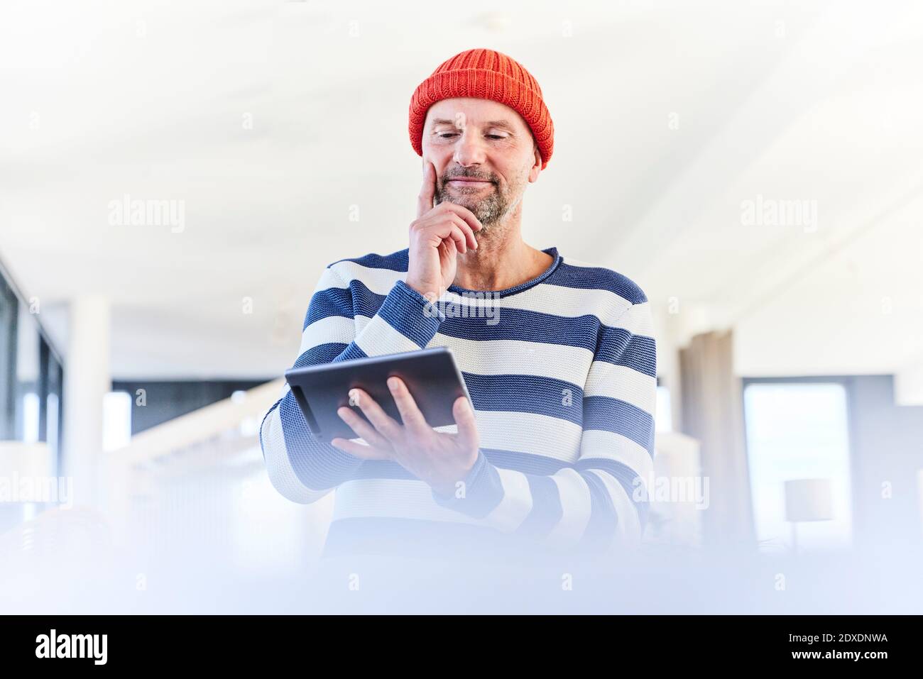 Thoughtful man using digital tablet while standing at home Stock Photo
