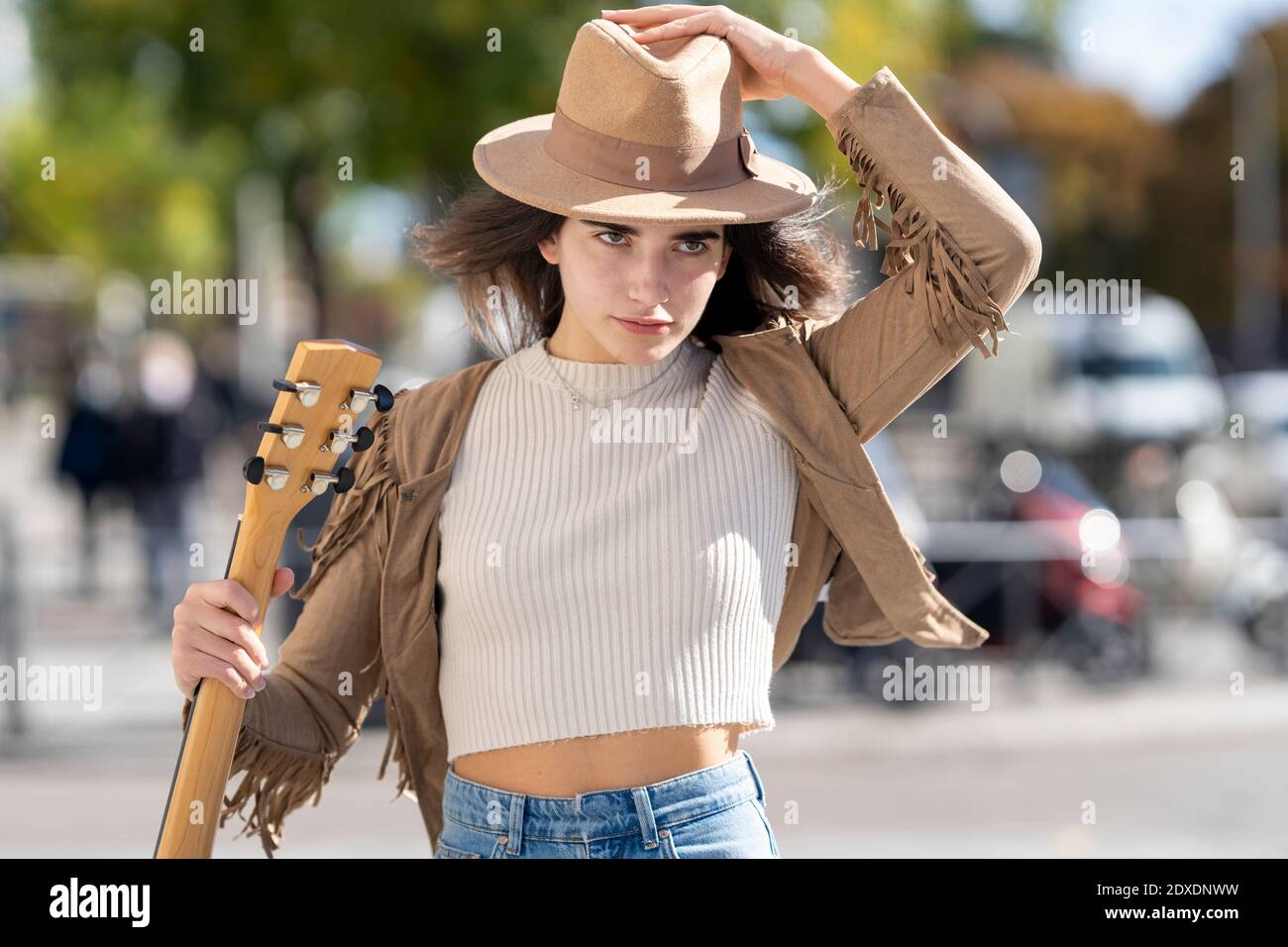 Young woman wearing hat and holding guitar on sunny day Stock Photo