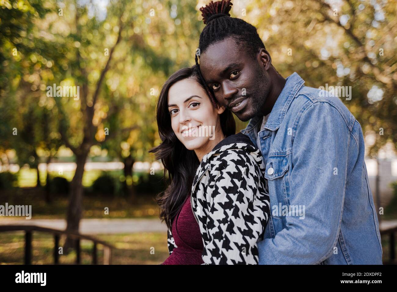 Smiling multi ethnic couple embracing while standing in park Stock Photo