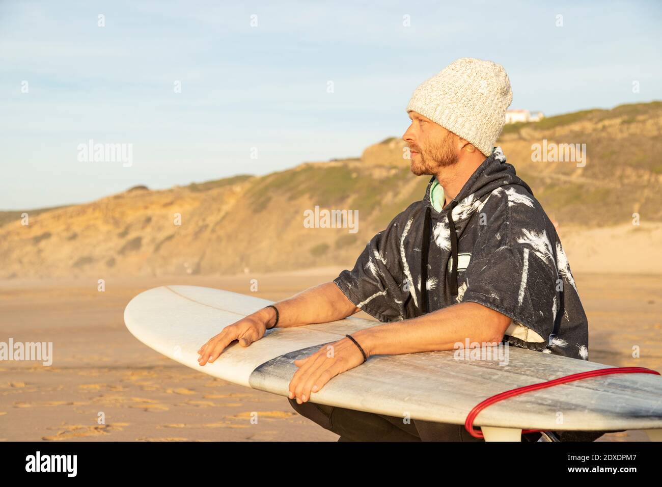 Man looking away while crouching with surfboard at beach Stock Photo