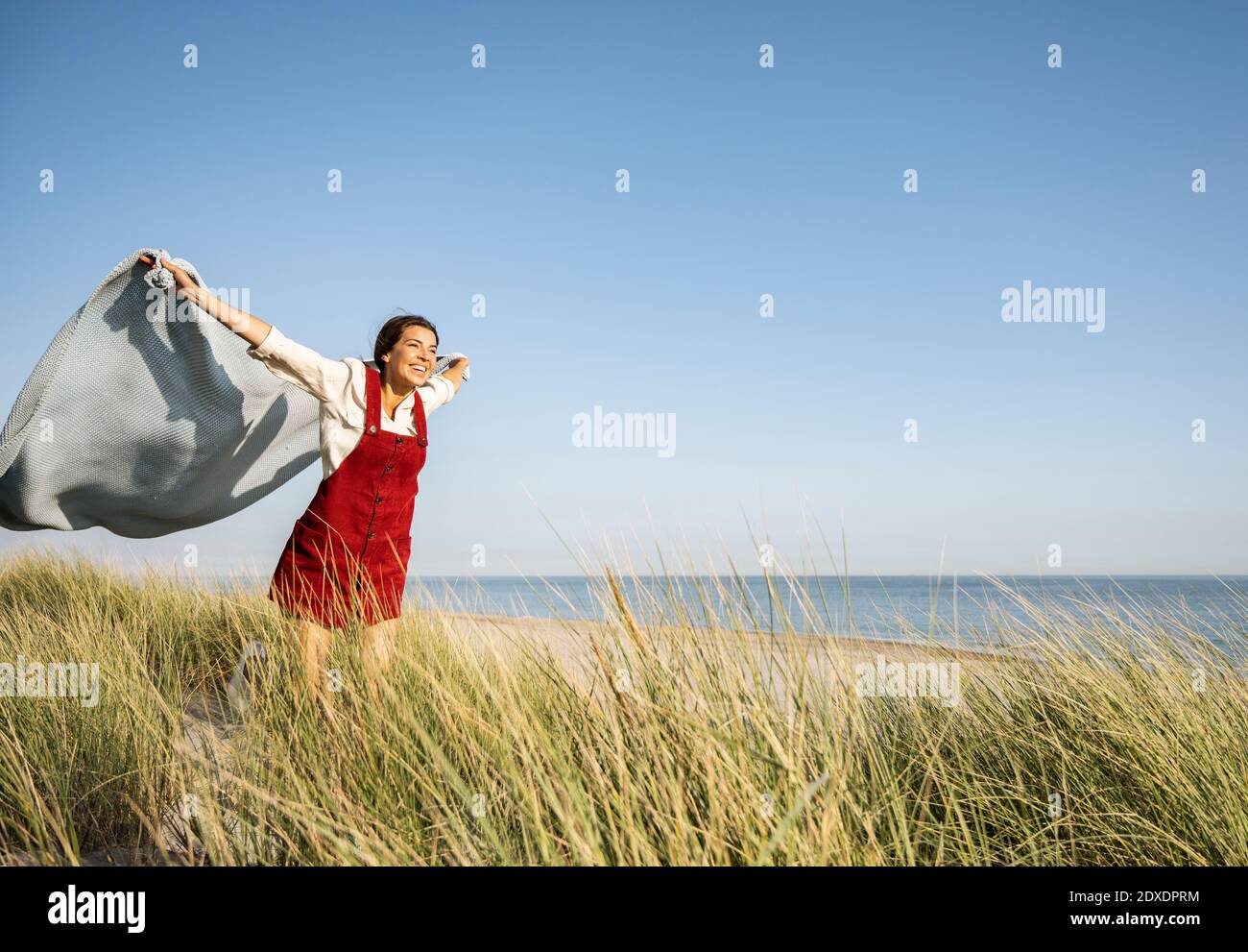 Young woman with arms outstretched holding shawl while standing at beach Stock Photo