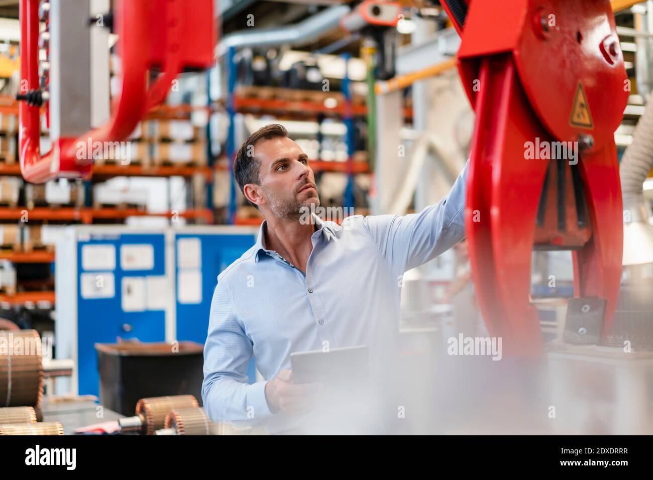 Businessman examining claw machine while holding digital tablet standing in factory Stock Photo