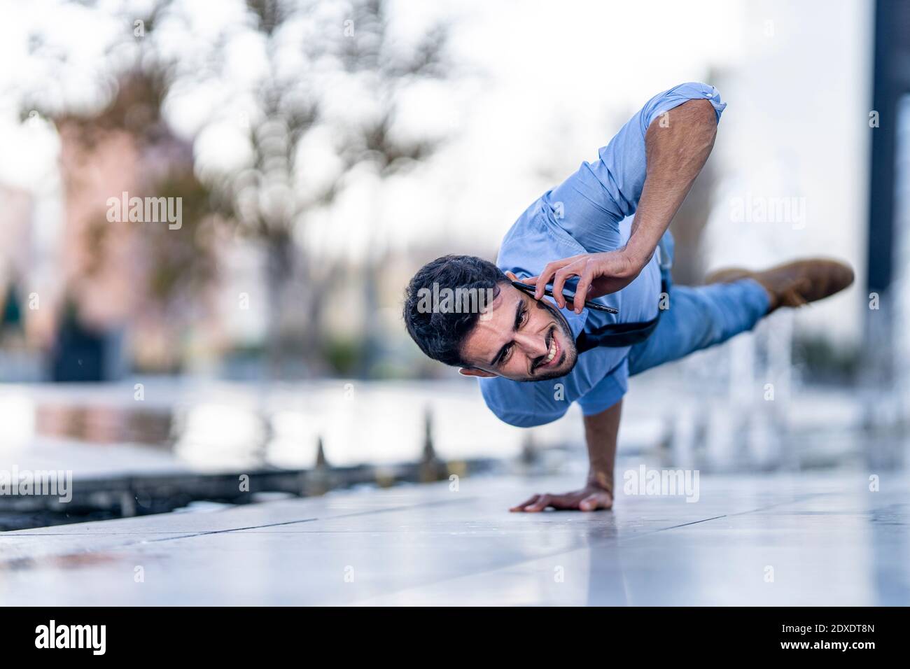 Businessman talking on mobile phone while doing handstand on footpath Stock Photo
