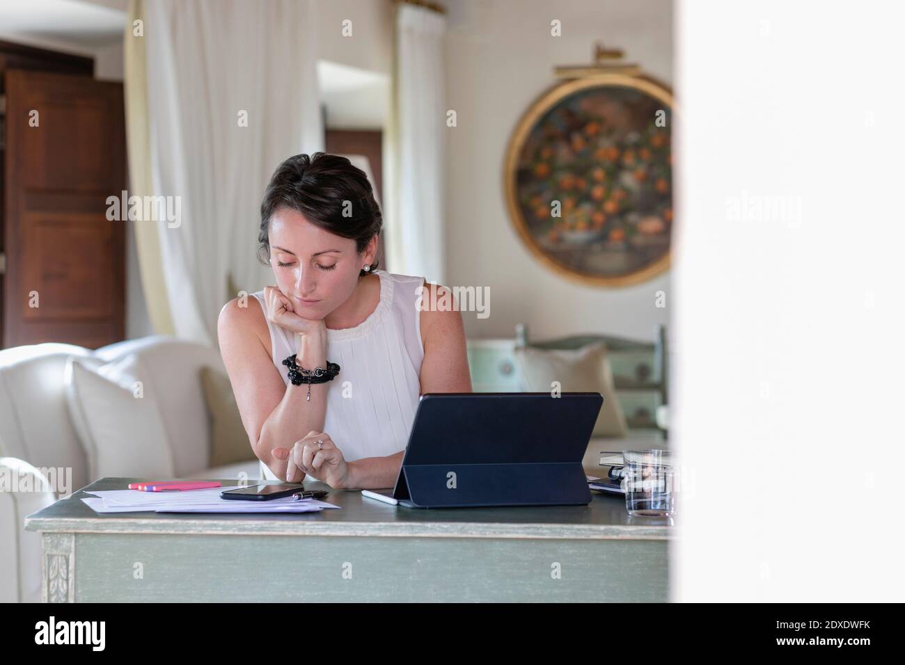 Businesswoman with hand on chin using smart while working at home Stock Photo