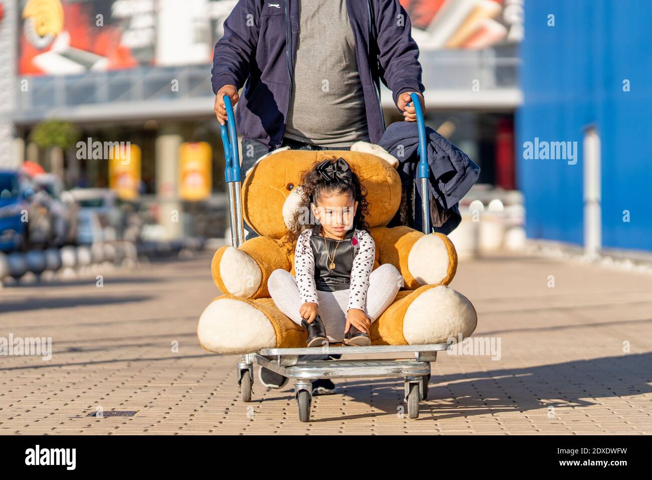 Cute girl sitting with teddy bear in luggage cart on footpath Stock ...