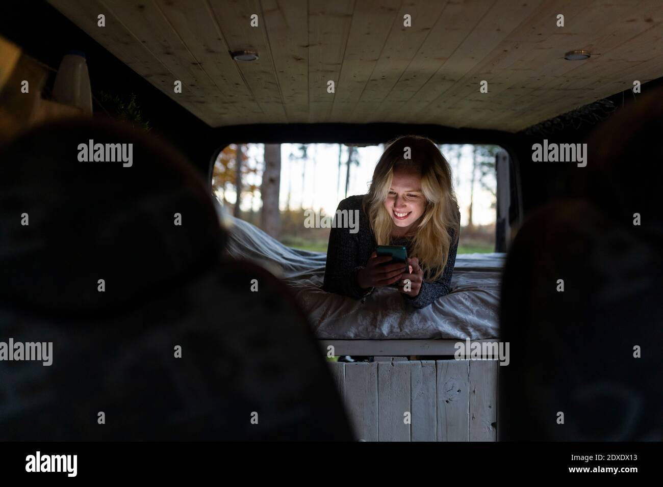 Happy woman on bed using smart phone in camper van Stock Photo