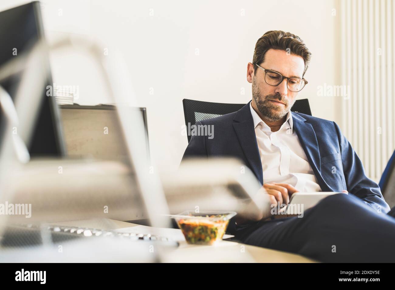 Businessman using mobile phone while having lunch sitting at office Stock Photo