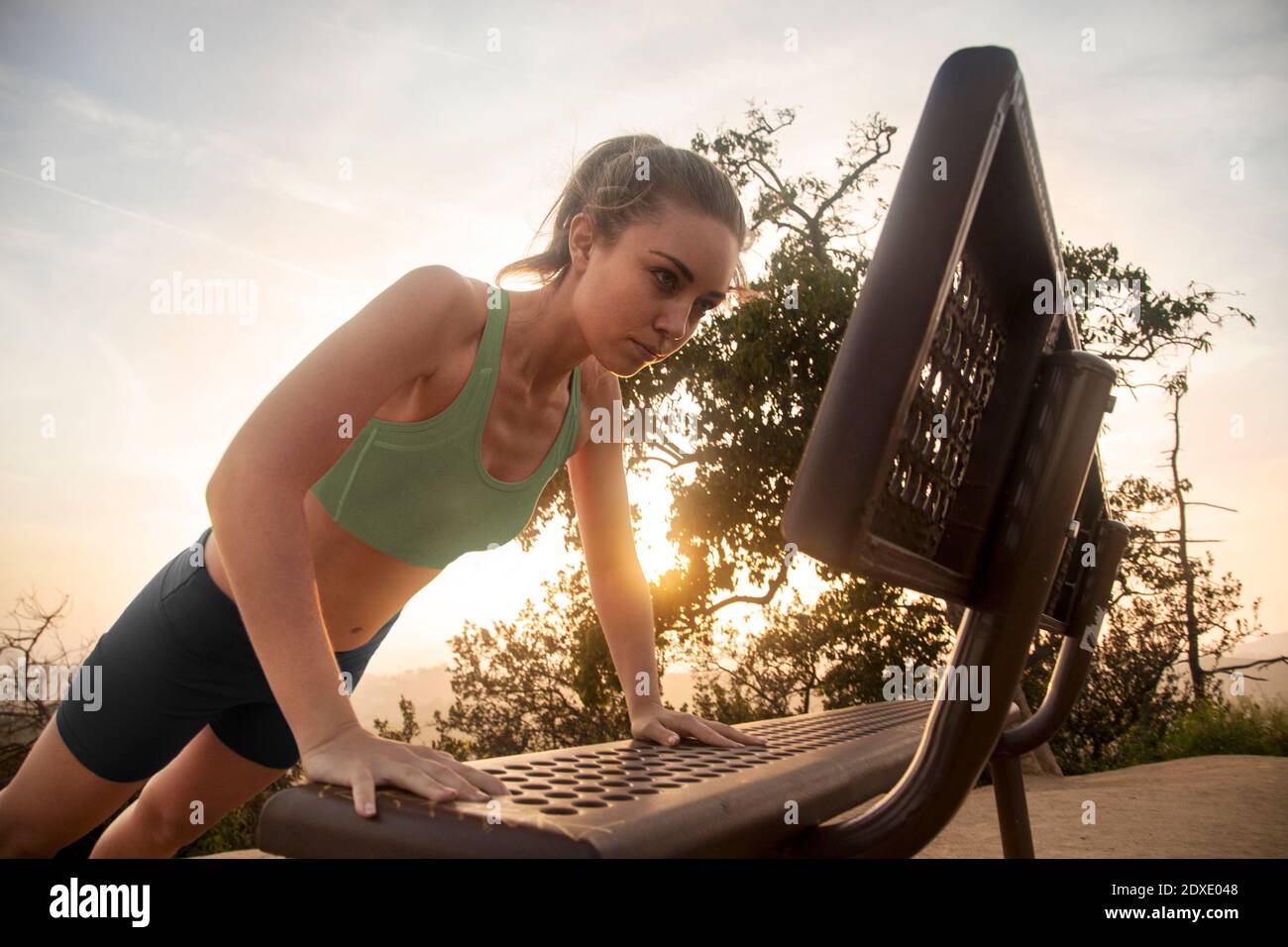 Sportswoman exercising while doing push-ups on bench against sky Stock Photo