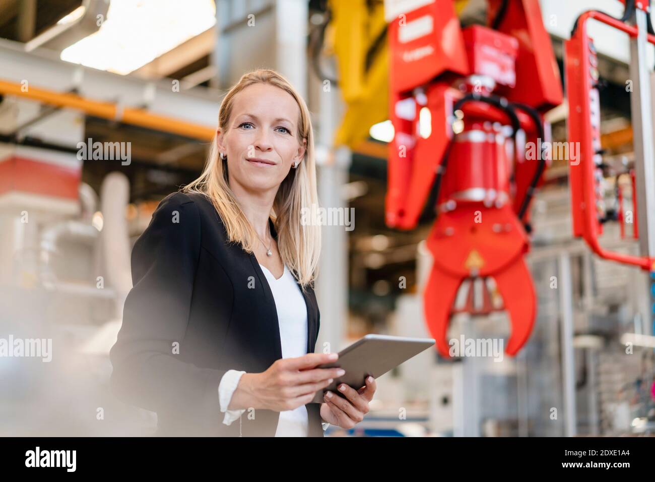 Smiling businesswoman holding digital tablet standing in industry Stock Photo