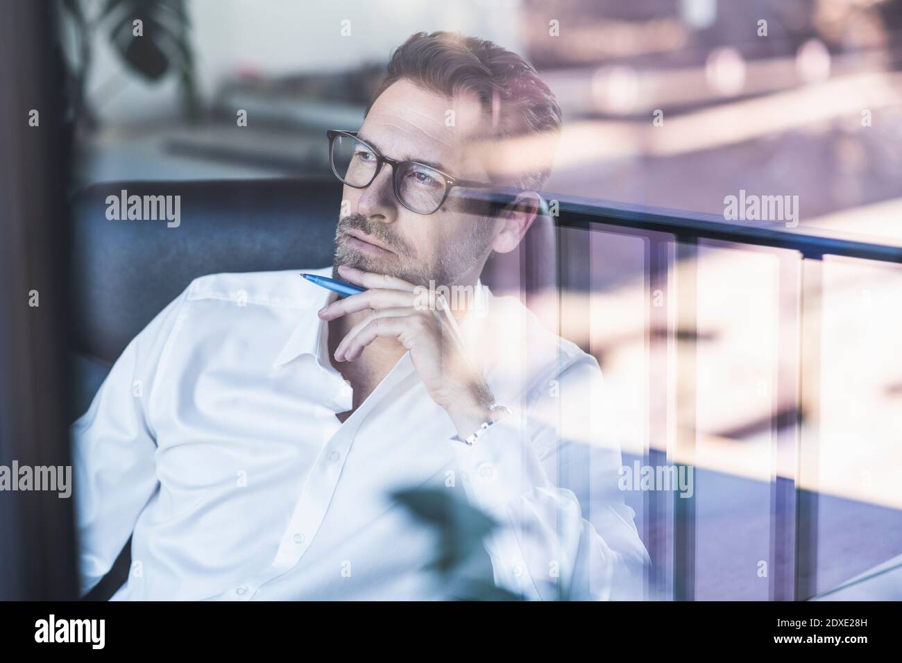 Thoughtful mature businessman looking away sitting with hand on chin at office Stock Photo