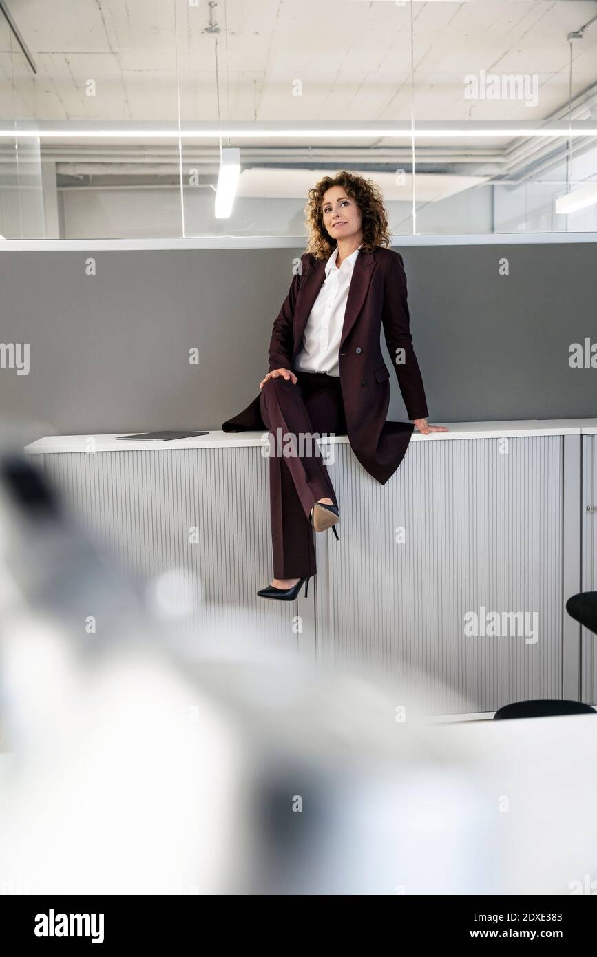 Confident businesswoman sitting with legs crossed at knee on tablet in office Stock Photo