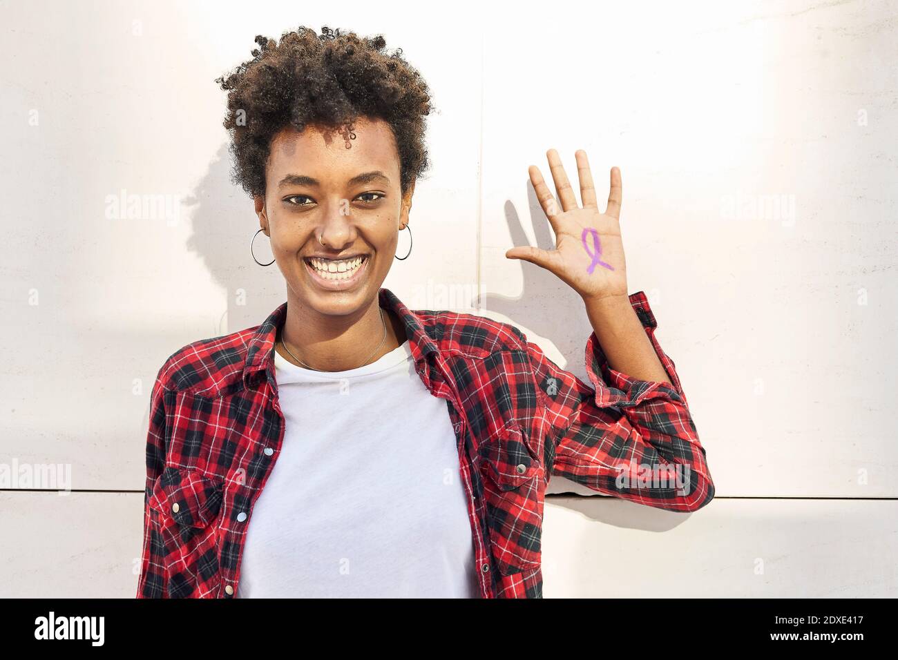 Cheerful young woman with purple awareness symbol on palm against white wall during Womens Day Stock Photo