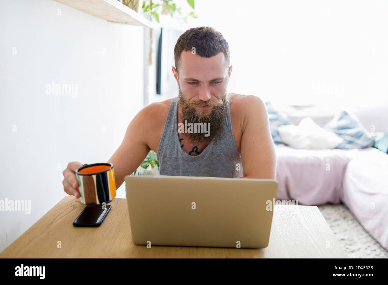 Bearded man using laptop while holding coffee cup at home Stock Photo