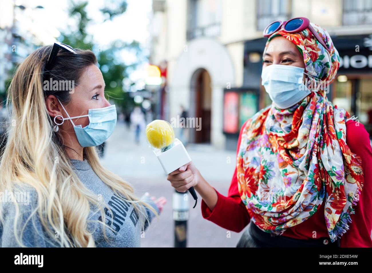Female journalist interviewing woman with microphone in city during COVID-19 Stock Photo