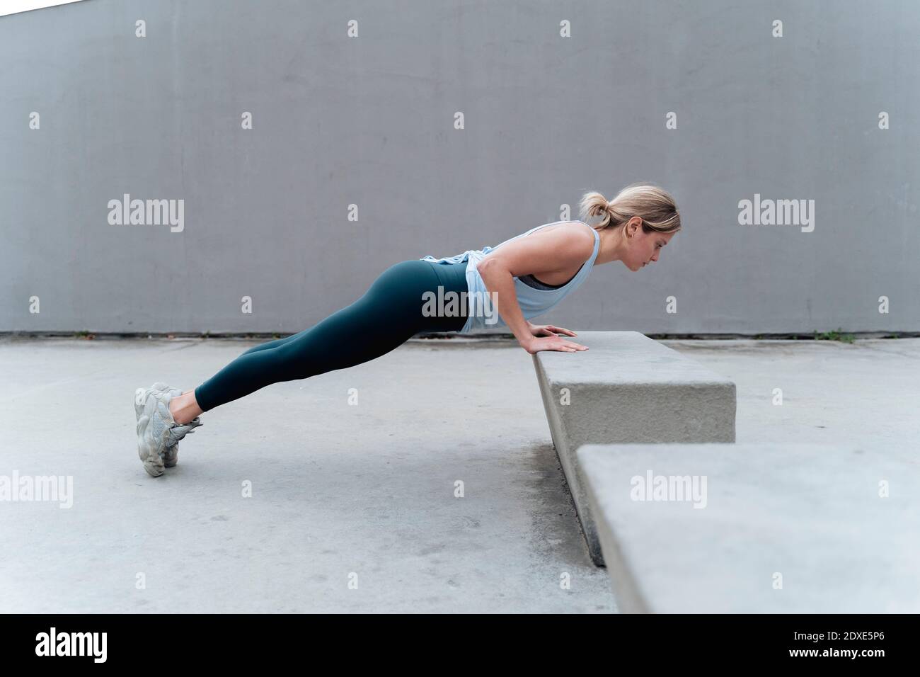 Sportswoman doing push-ups while exercising against wall Stock Photo