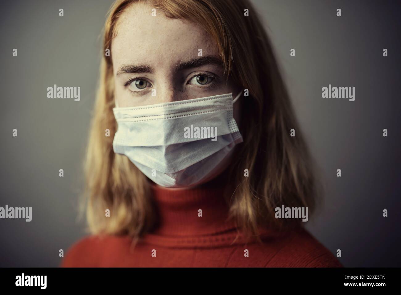 Teenage girl wearing protective face mask while standing against gray background Stock Photo