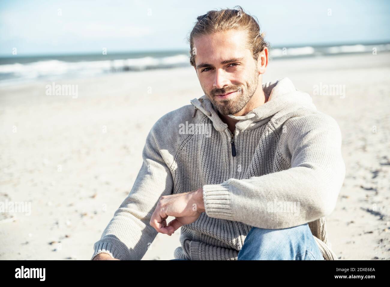 Smiling man sitting with hand on knee at beach Stock Photo