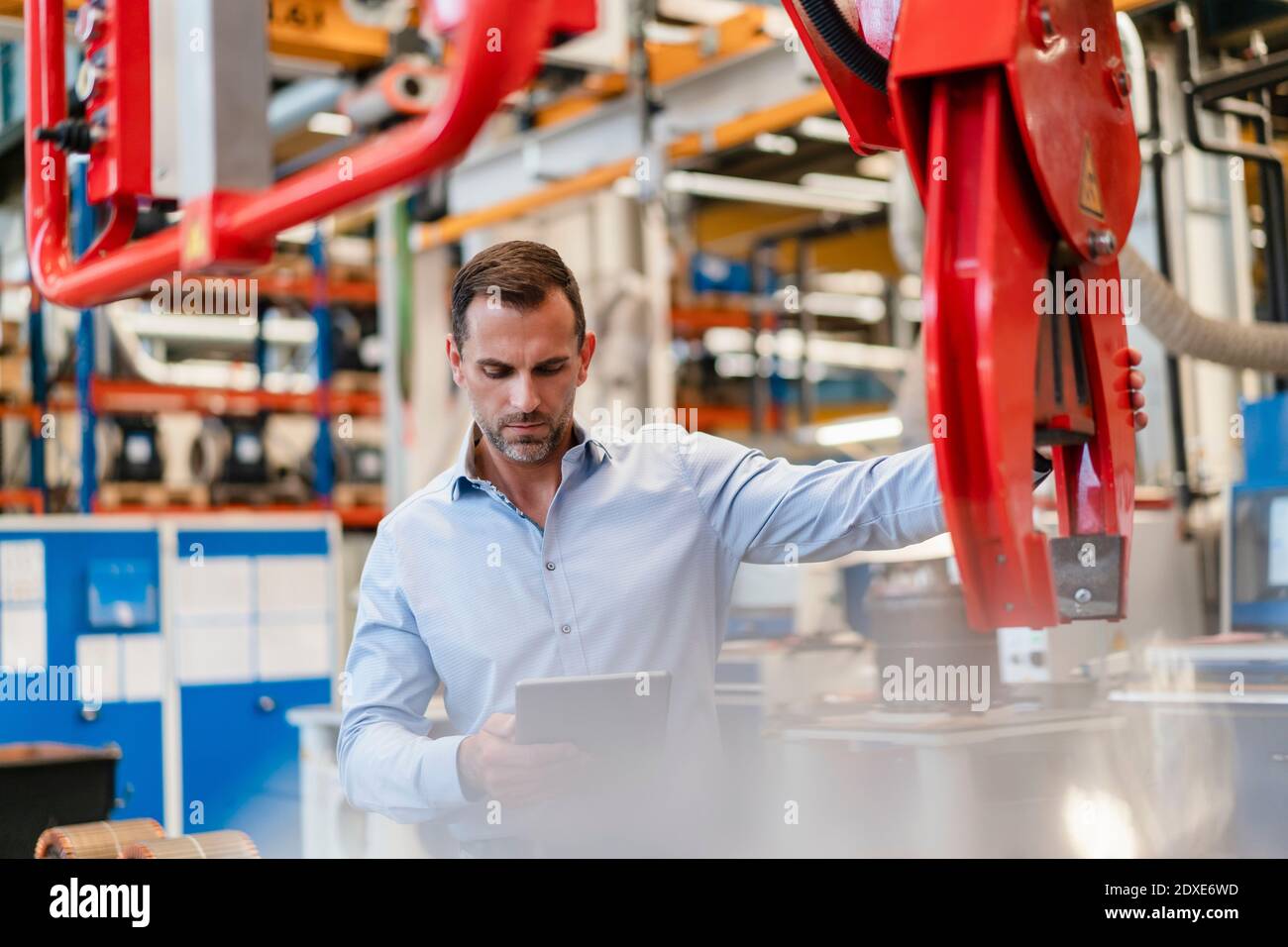 Male entrepreneur analyzing claw machine while using digital tablet standing in factory Stock Photo
