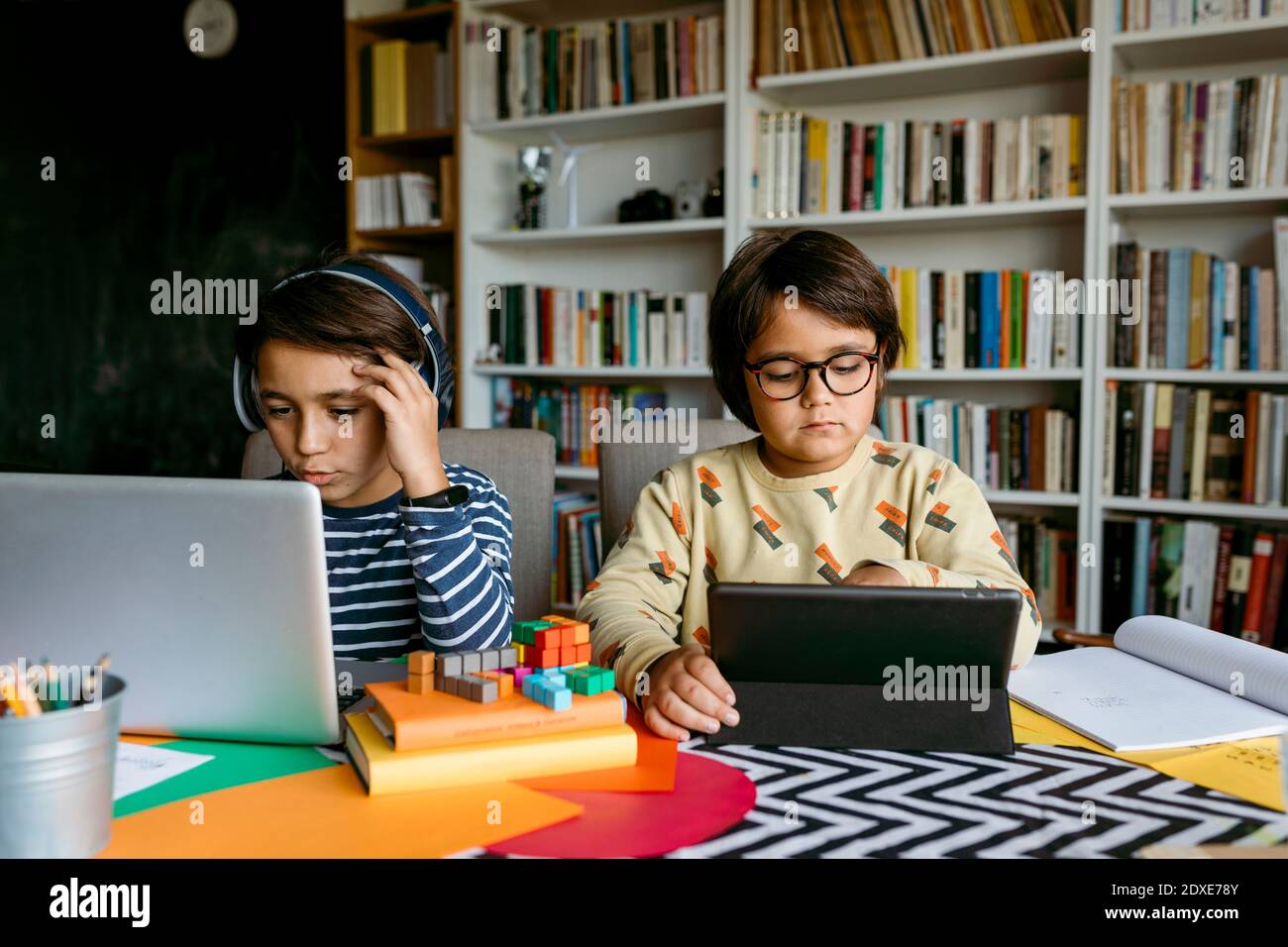 Boy e-learning through laptop while male friend studying with digital tablet at table Stock Photo