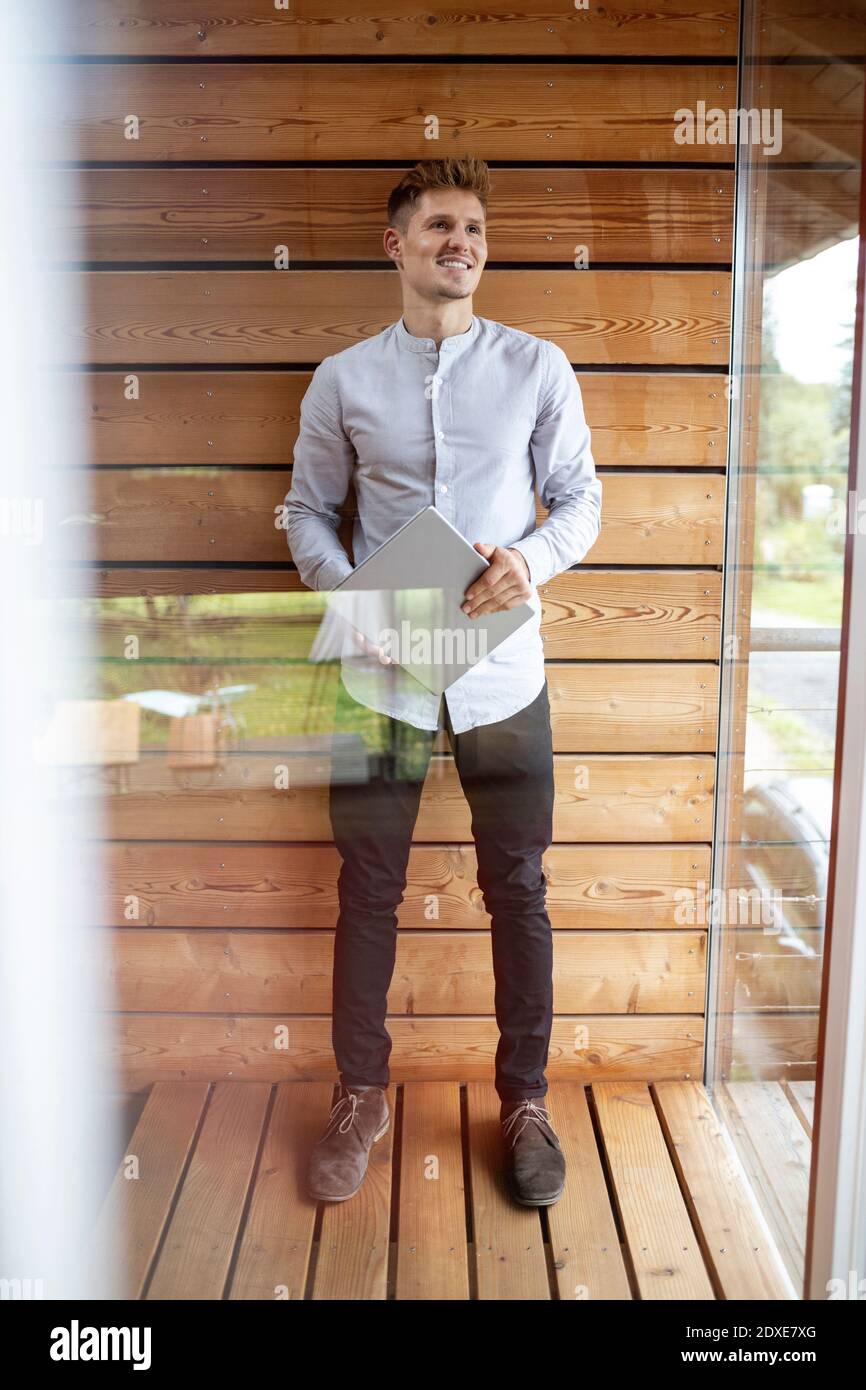 Smiling man holding digital tablet while standing at home Stock Photo