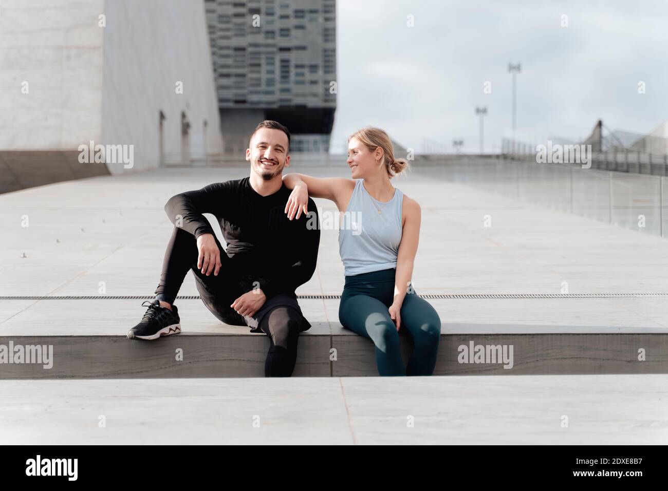 Couple smiling while sitting by retaining wall Stock Photo