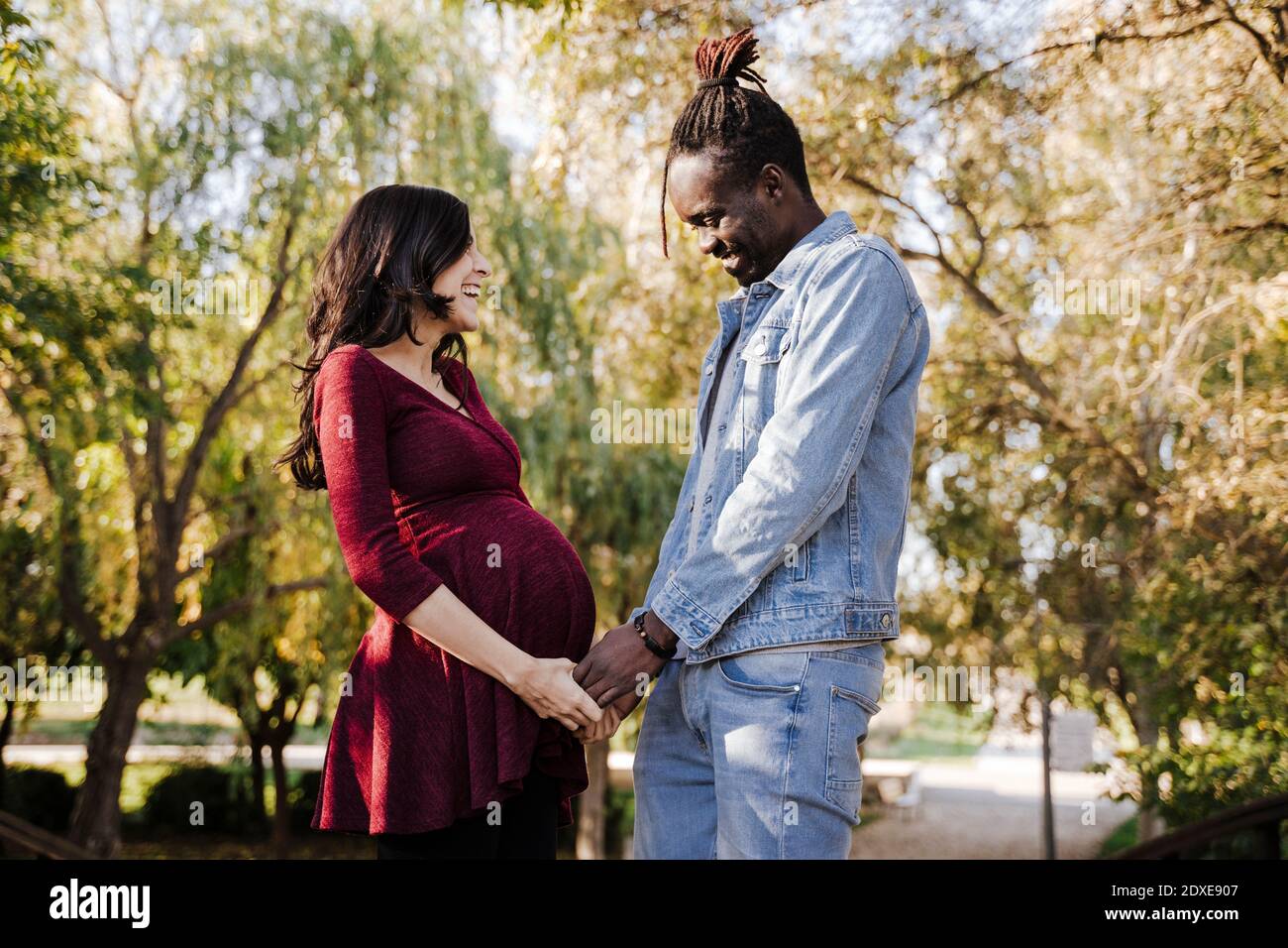 Happy man looking at pregnant woman's stomach in park Stock Photo