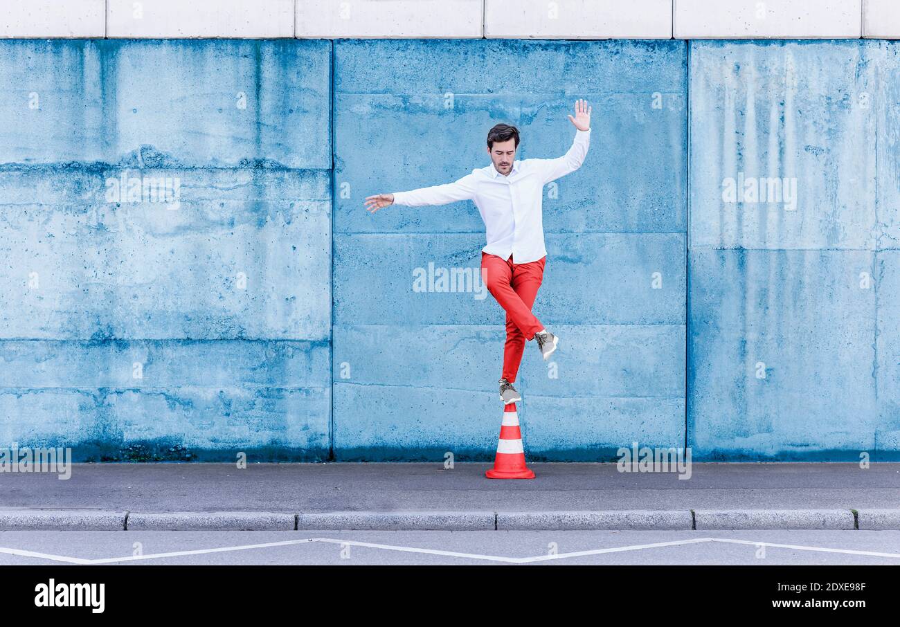 Man balancing while standing on traffic cone against blue wall Stock Photo