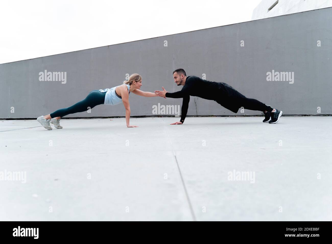 Young couple giving high-five while doing plank against wall Stock Photo