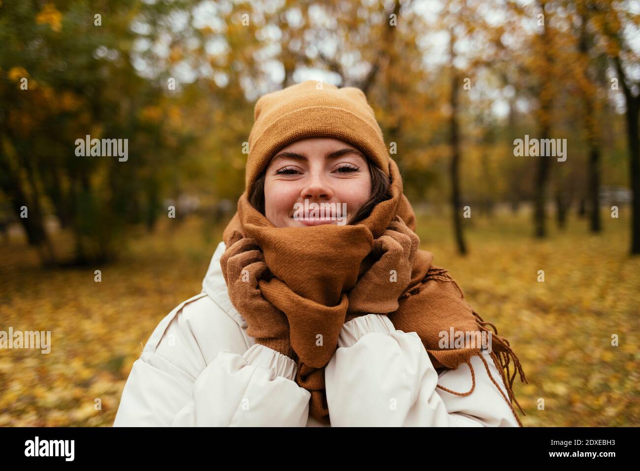Smiling young woman wrapped up in scarf in autumn park Stock Photo