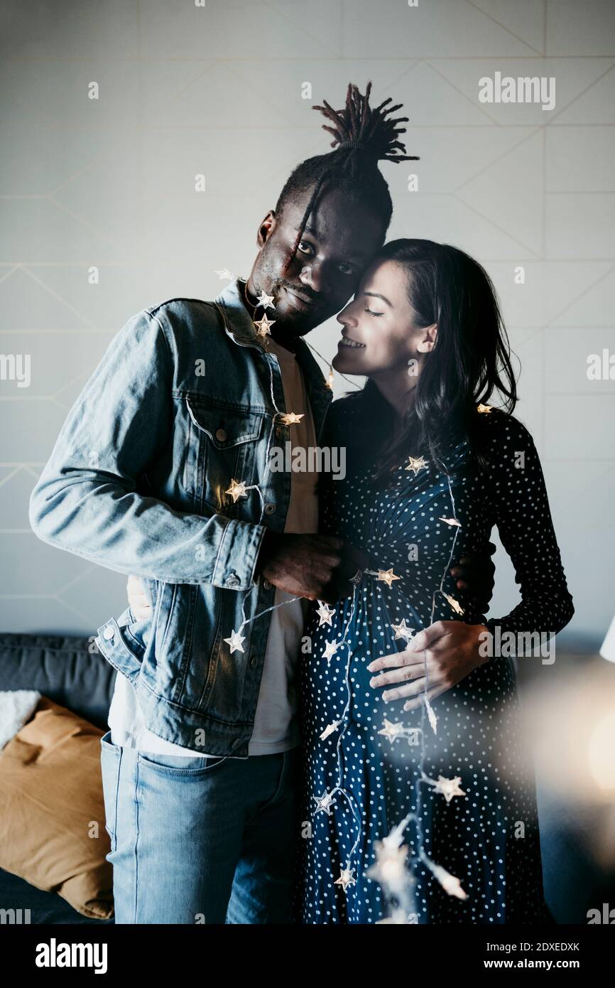 Young man and smiling pregnant woman with star shaped lights at home Stock Photo