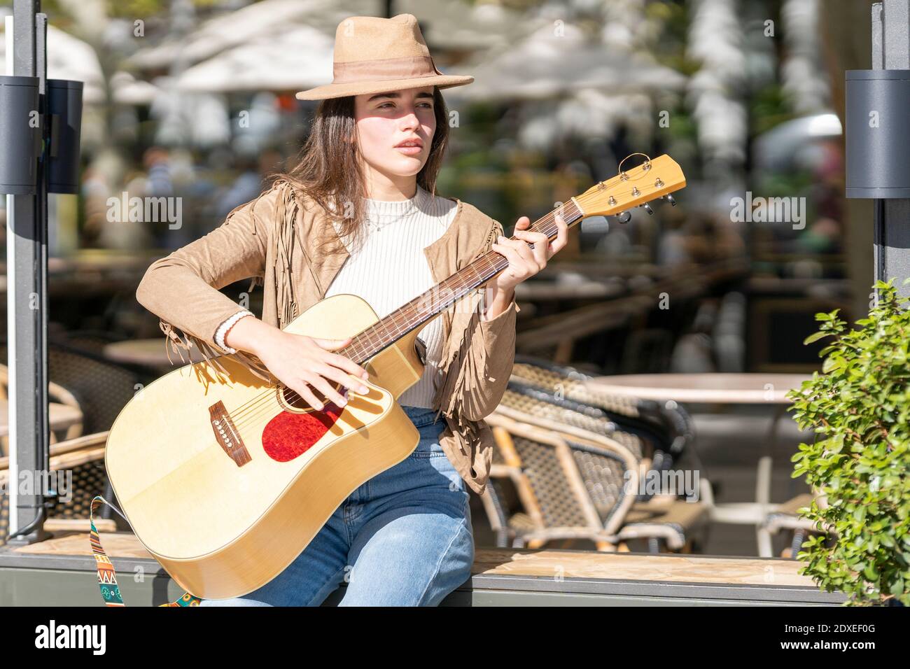 Young woman playing guitar while sitting on bench during sunny day Stock Photo