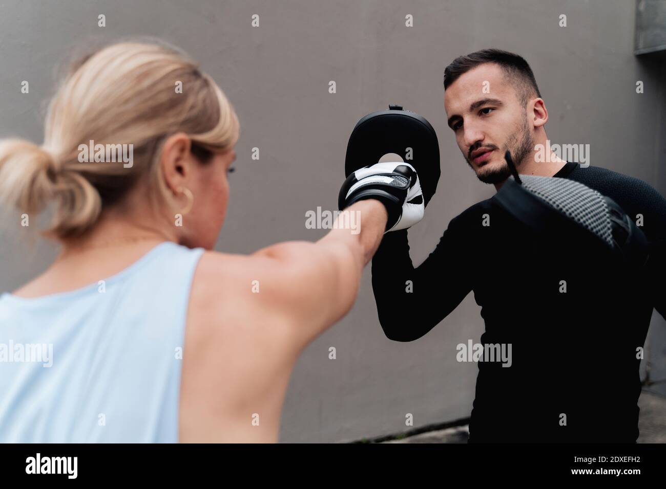 Sportswoman sparring with man while standing against wall Stock Photo