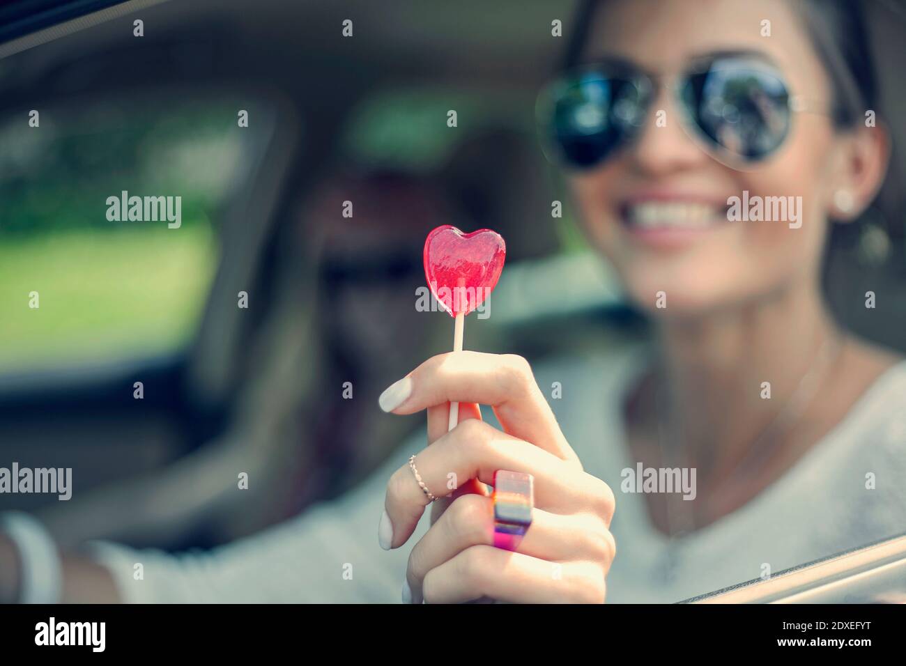 Happy young woman showing heart shape lollipop during road trip Stock Photo