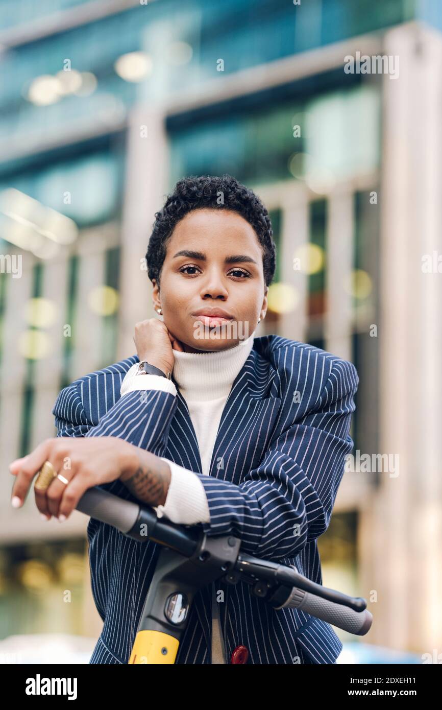 Confident young businesswoman leaning on handlebar of electric push scooter Stock Photo