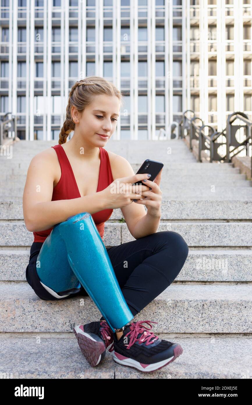 Sportswoman with prosthetic leg smiling while using mobile phone