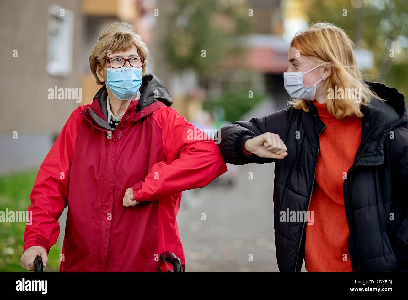 Granddaughter and mother wearing face mask greeting with elbow bump while standing outdoors Stock Photo