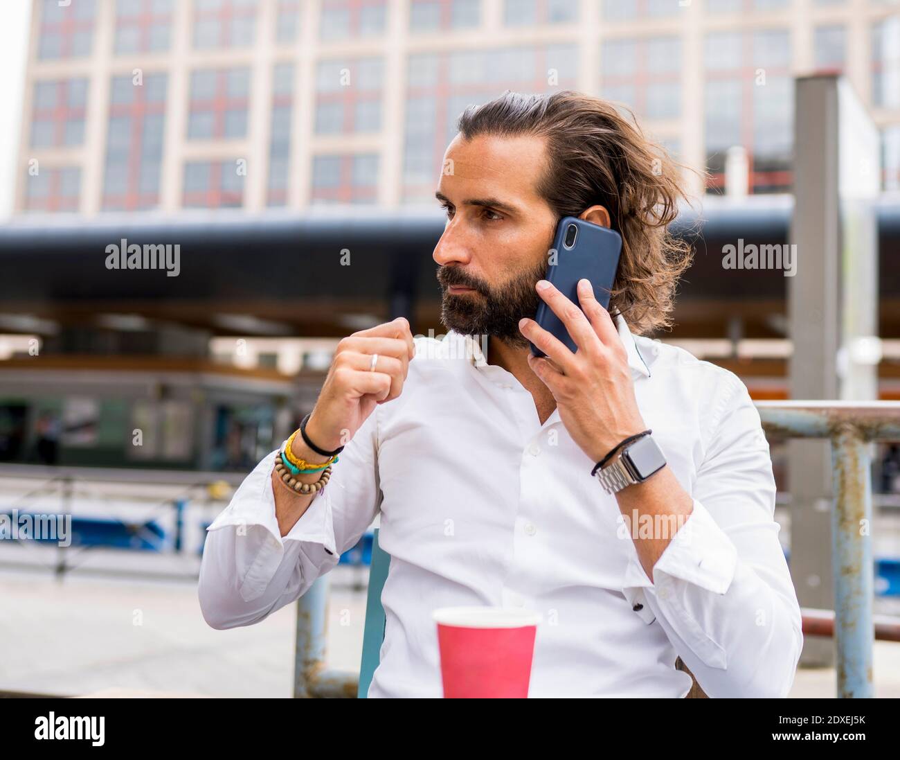 Candid portrait of bearded businessman sitting outdoors and talking on smart phone Stock Photo