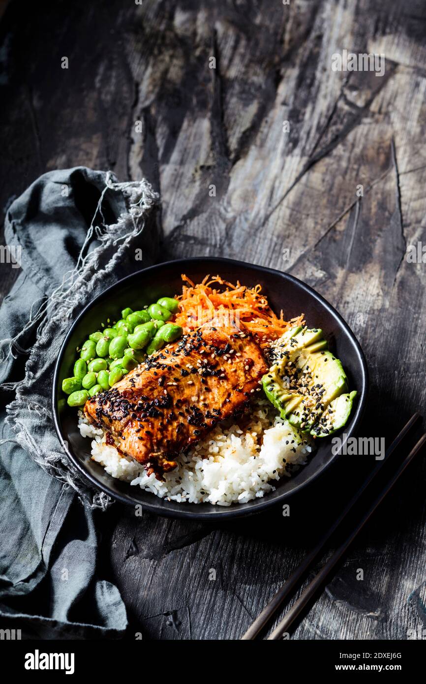 Bowl of teriyaki salmon with rice, carrot salad, edamame beans, avocado