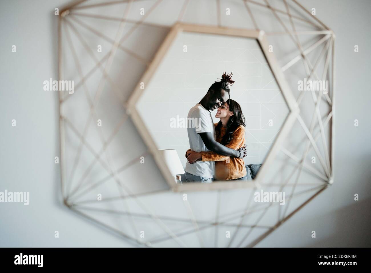 Reflection of multi-ethnic couple embracing on mirror at home Stock Photo